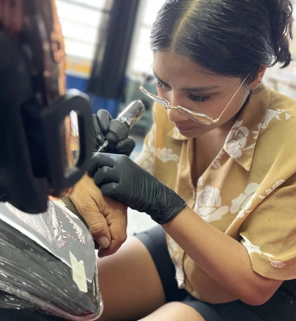 Jacky Lossan tatuando con guantes y máquina de bobinas en su estudio de tatuajes en Tláhuac, CDMX